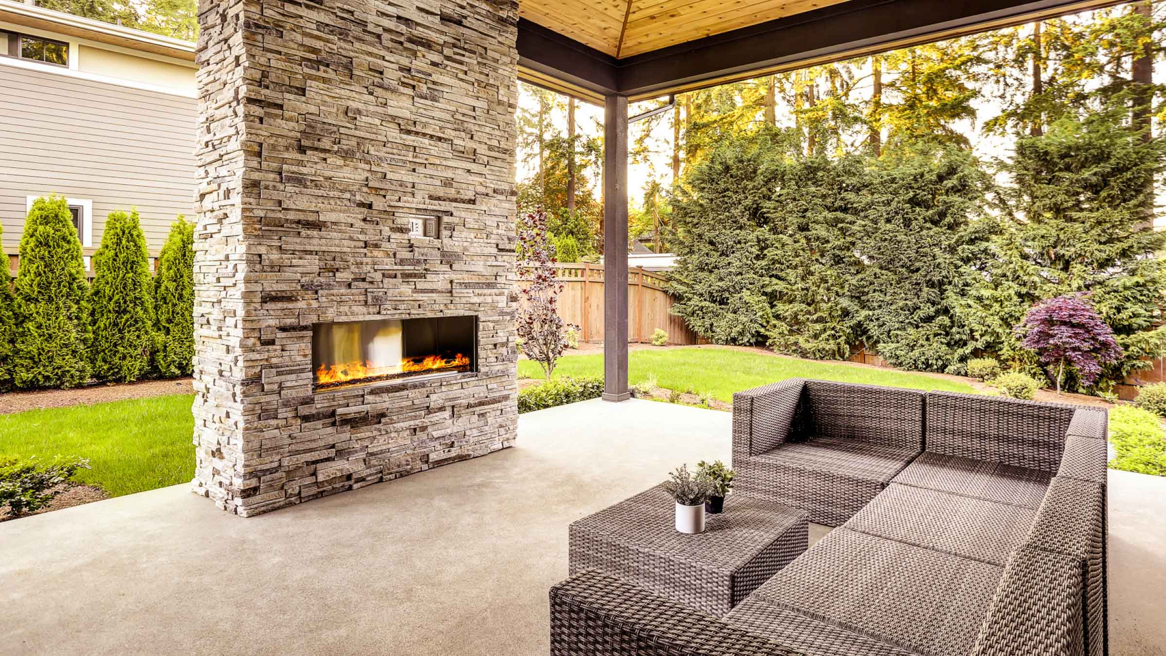 Modern outdoor entertainment area, with glass front fireplace mounted on stonework column.