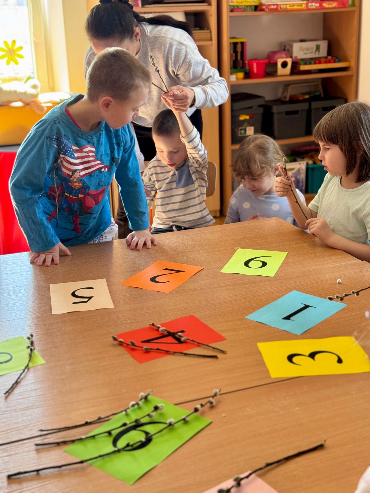 Rosnę z matematyką | Dzieci ptzuy stoliku na którym leżą kolorowe kartki z numerami.jpg
