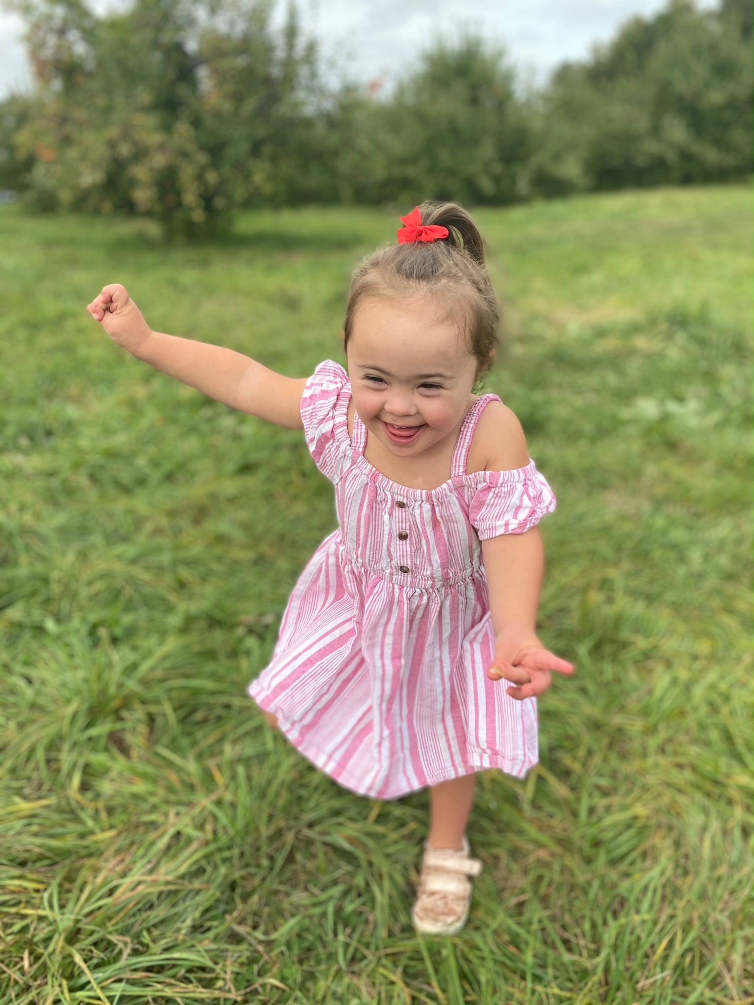 A young girl with down syndrome smiling as she runs through a field of grass