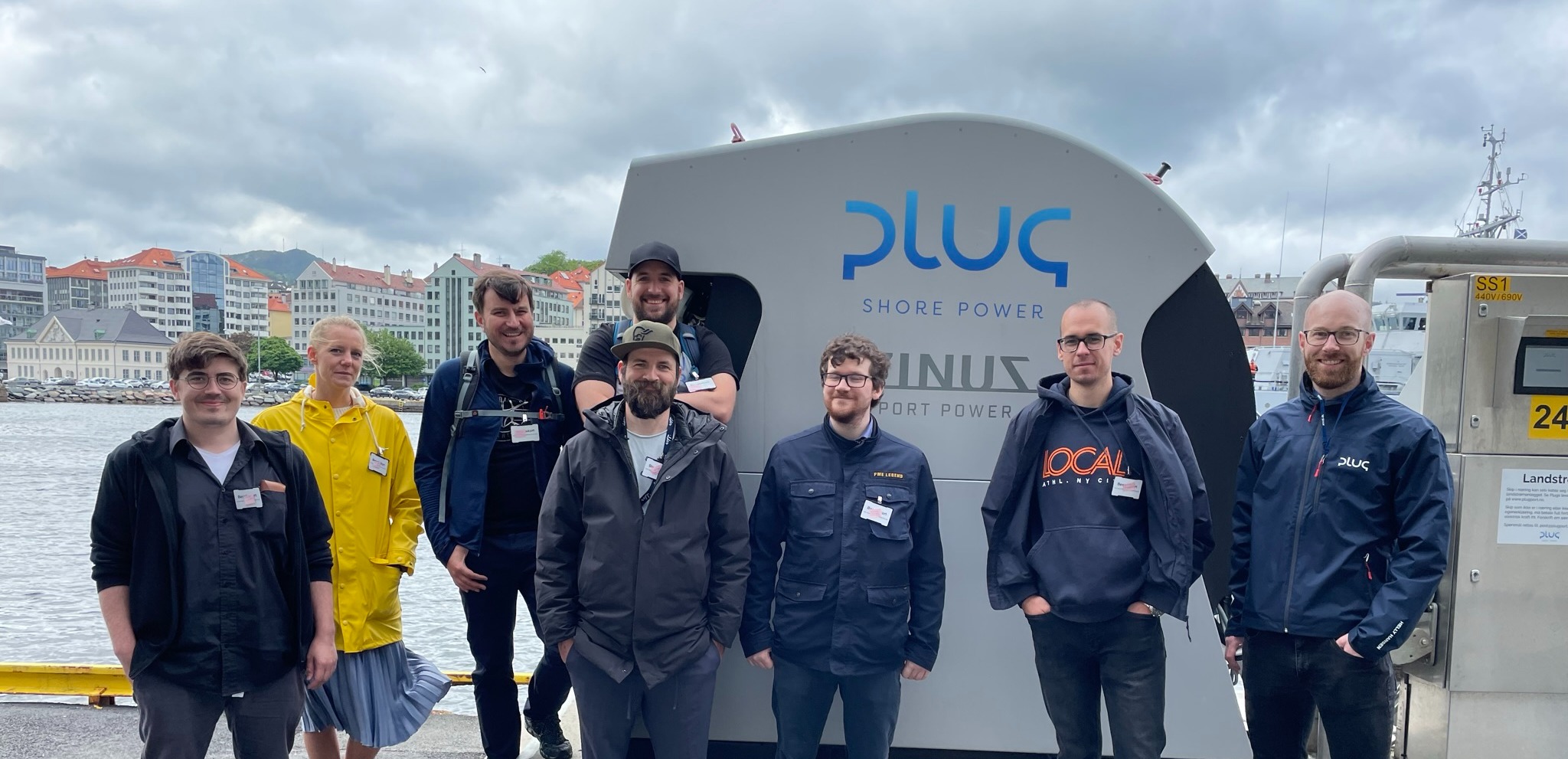 Bilde av ansatte i Ilder foran Plug logoen i Bergen