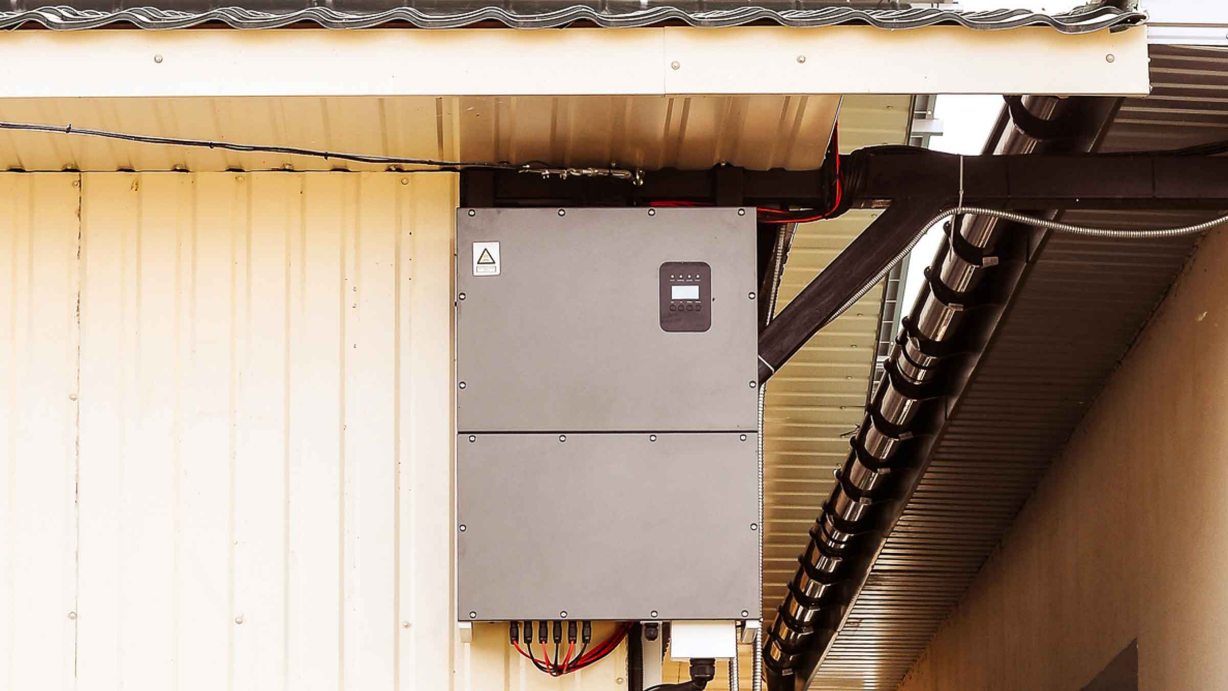 Outside view of a small corner of a timber frame home. A grey battery is attached to the home, just below its roof.