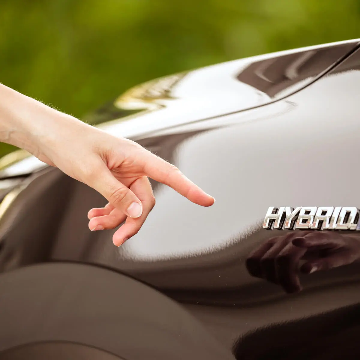 Hand reaches our pointing towards a black hybrid electric vehicle, which has the word 'hybrid' written on it.