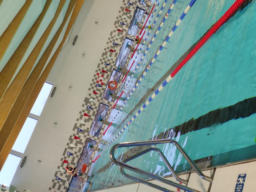 Zajęcia feryjne | Kryty basen - widok ogólny. Z boku widoczna drbinka basenowa, na środku czerwone pływaki wyznaczające tory.jpg