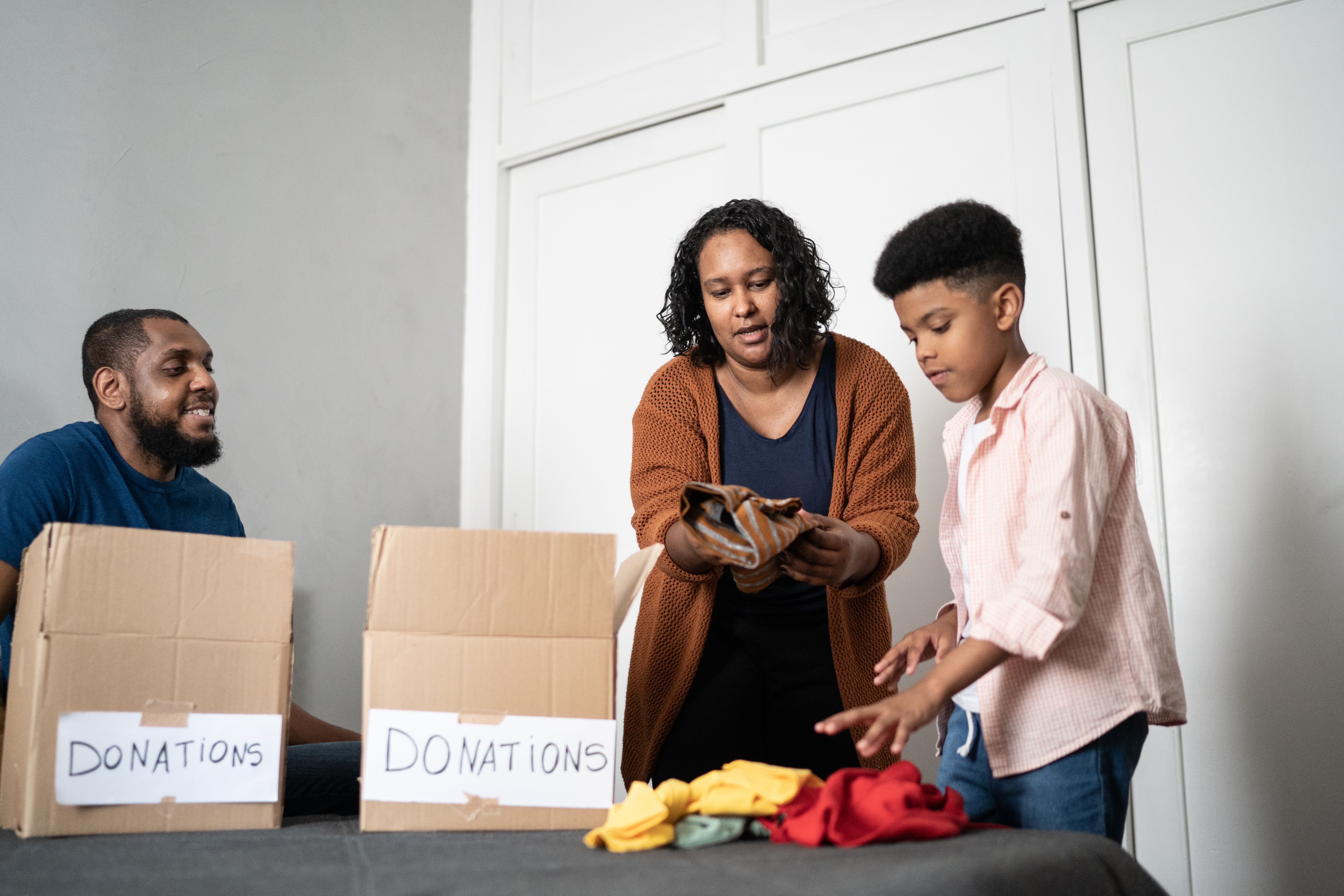 Parents with son sorting out clothes in boxes to donate at home