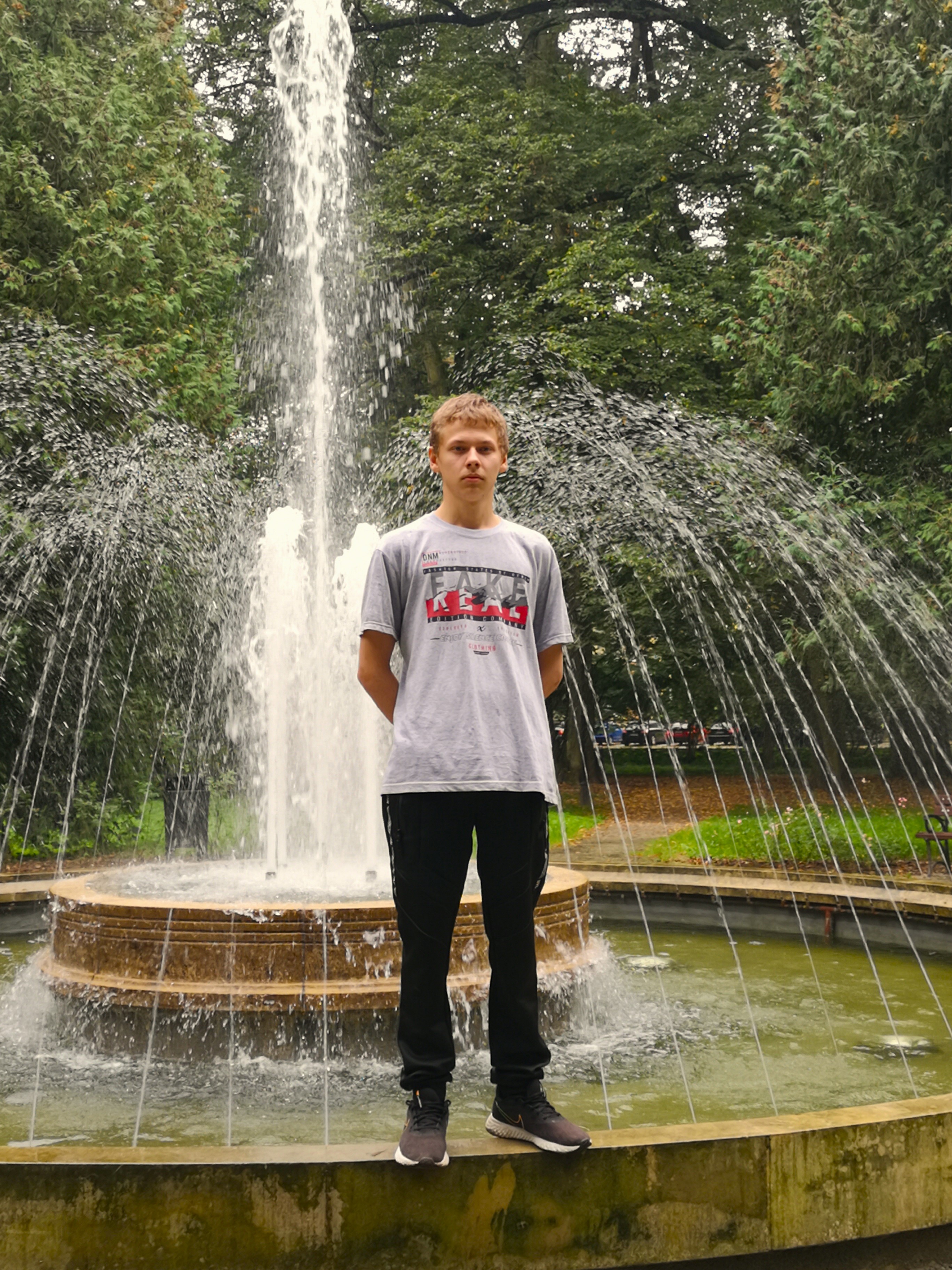 Wycieczka do Jarosławia. | Wychowanek MOW stojący na obrzeżu fontanny, w tle tryskająca woda, z tyłu gęste duże drzewa..jpg
