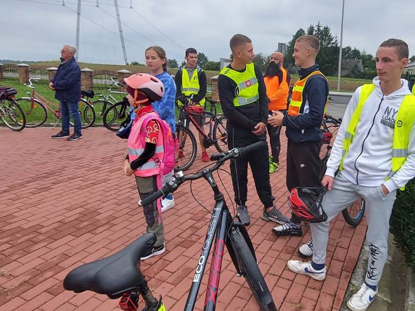Rajd rowerowy | Wychowankowie MOW i inni uczestnicy rajdu stoją na placu wyłożonym czerwoną kostką, między nimi rowery..jpg