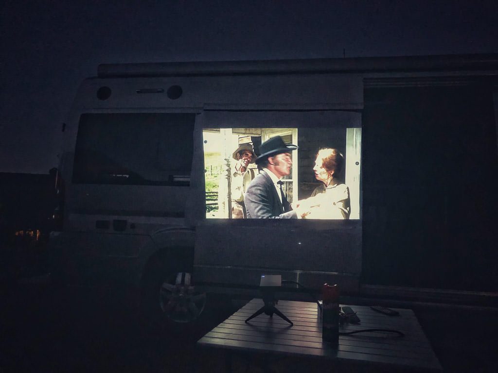 A movie playing on a projector on the side of an RV, one of the best camping ideas
