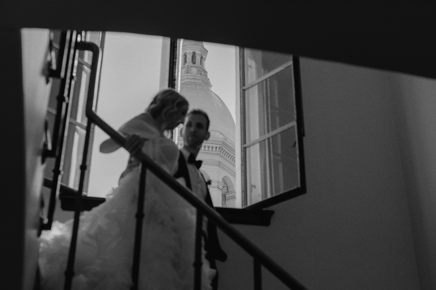 a bride and groom descend the stairs with a bell tower in the background in Downtown Los Angeles