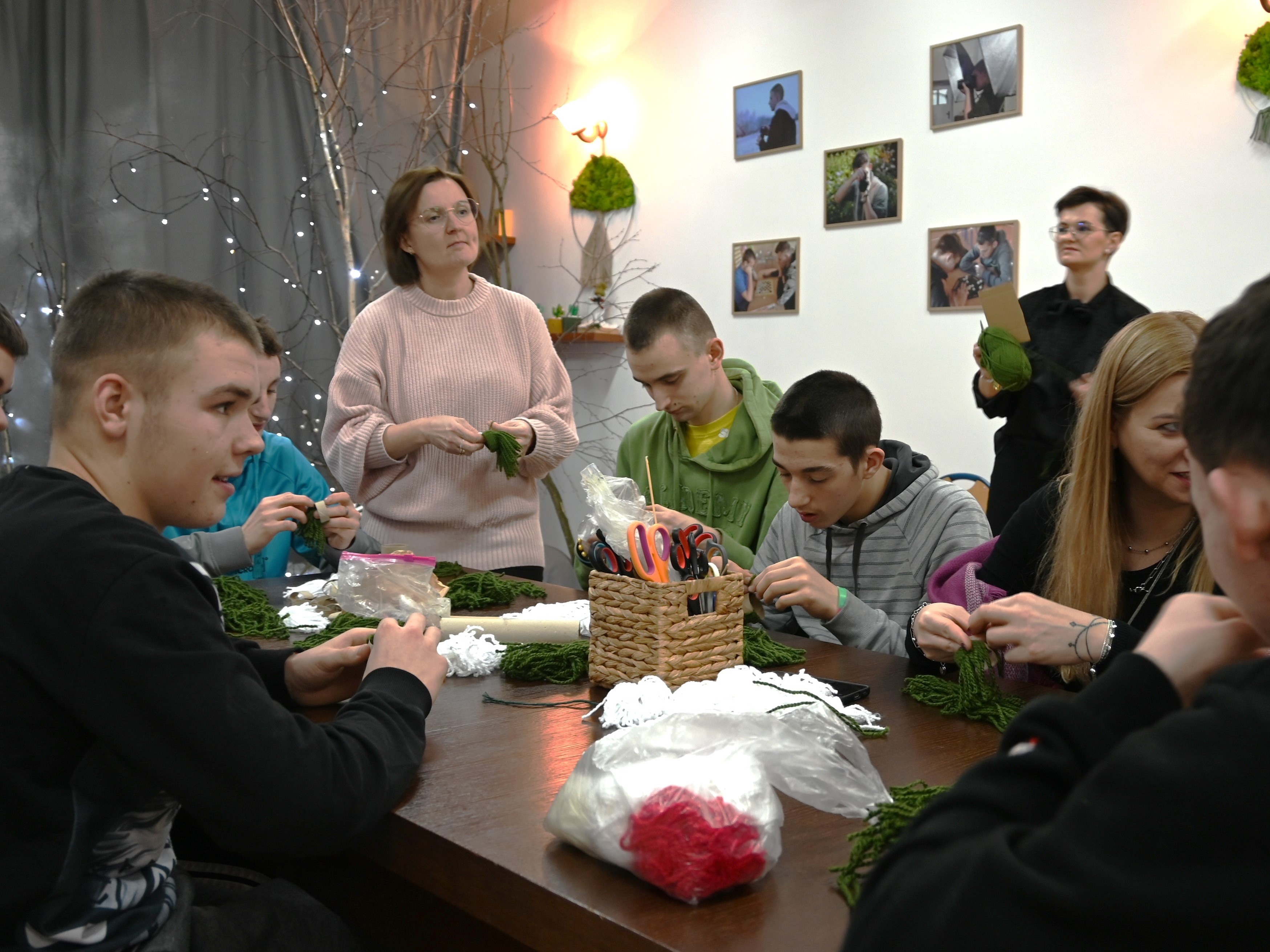Zakończenie projektu Fajna Ferajna | Młodzież podczas zajęć z wyplatania makram siedząca wokół stołu, na blacie kolorowe sznurki, koszyk z nożyczkami. Przy młodzieży stoją dwie wychowawczynie prowadzące zajęcia.JPG