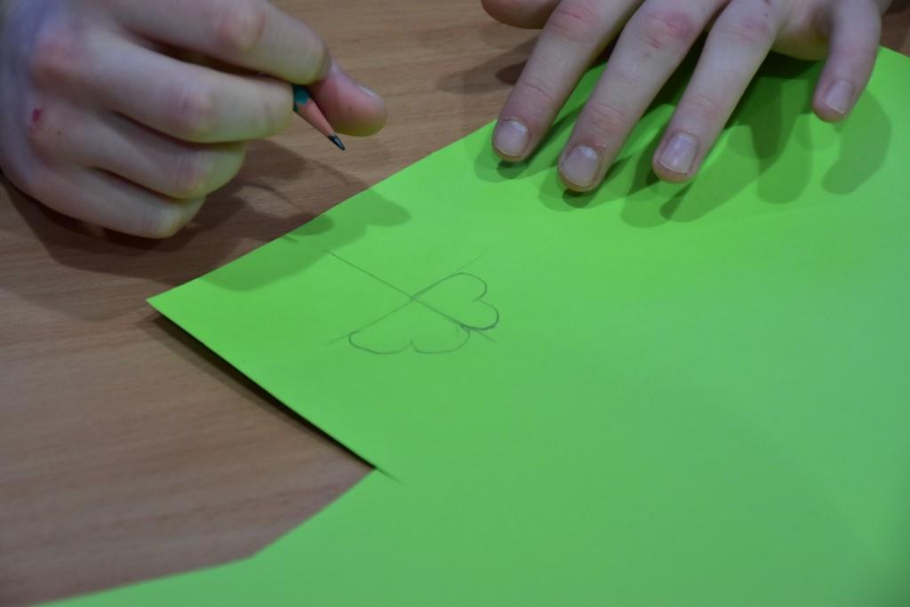 Dzień Św. Patryka  | Zielony karton, na którym czyjeś dłonie szkicują ołówkiem koniczynkę.JPG