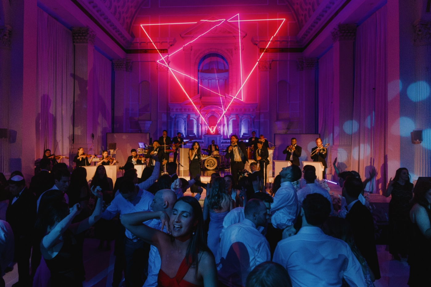 a band performs in front of a crowd in a cathedral wedding reception in Downtown Los Angeles with colorful lights