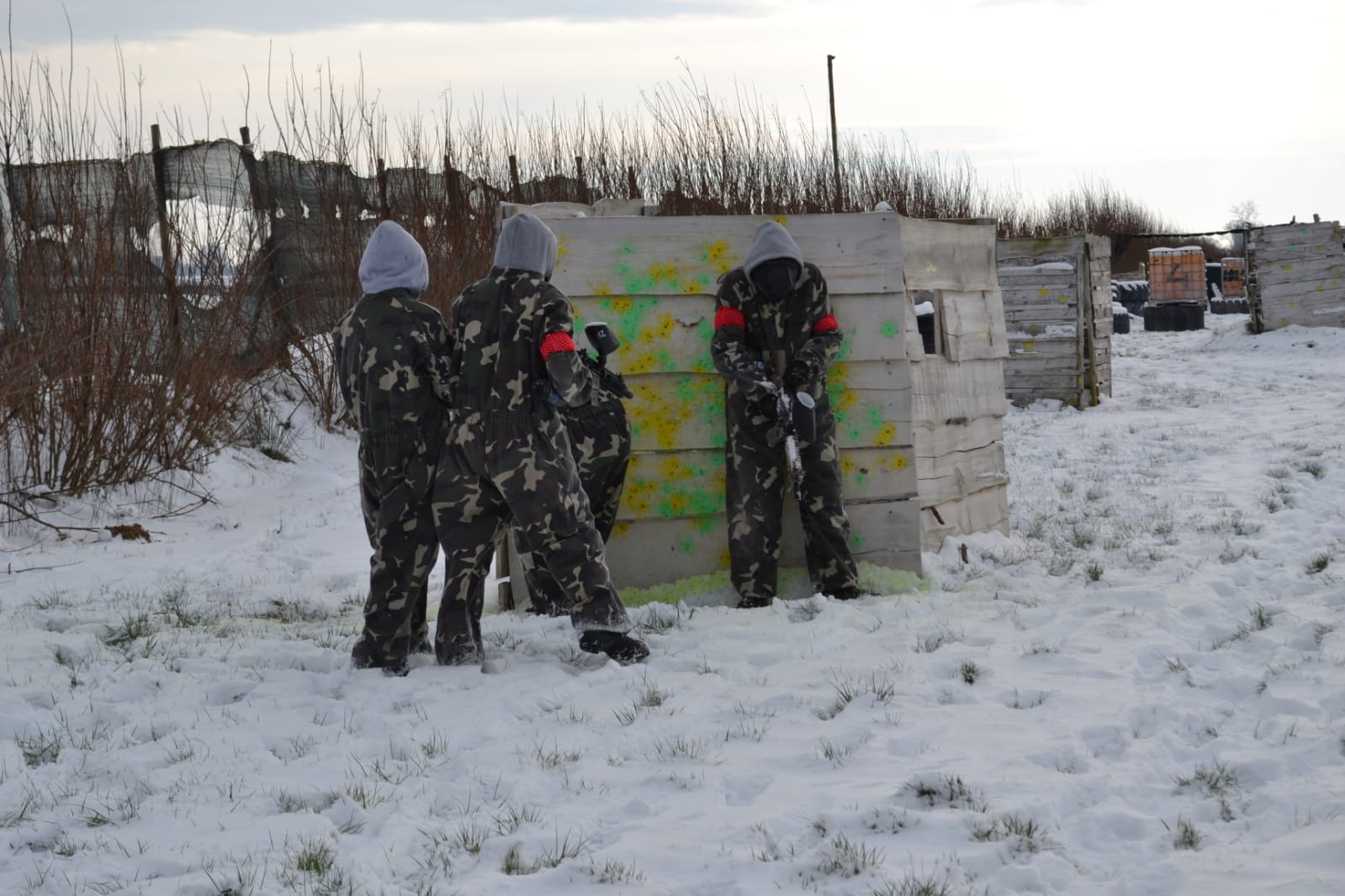 Wycieczka integracyjna klas Branżowej Szkoły I Stopnia w MOW w Lubaczowie | Cztery osoby w kombinezonach do paintballa, z karabinkami, chowają się za prowizoryczną ścianką z desek. Dookoła śnieg.jpg