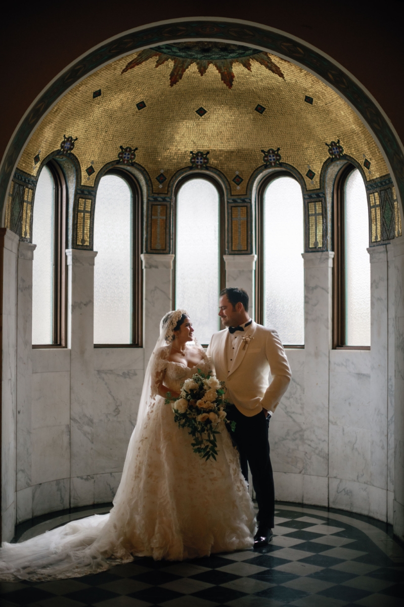 a bride and groom pose under the Vibiana gold dome in DTLA for their wedding