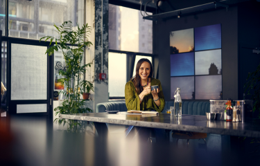 Woman sits smiling holding a coffee mug.