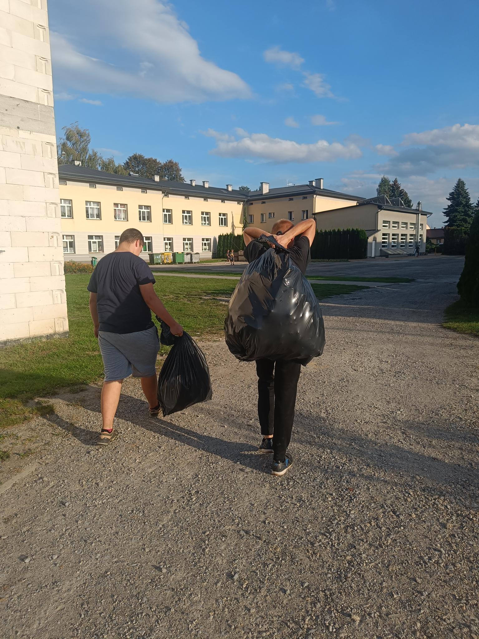 Sprzątanie świata | Dwóch wychowanków MOW wraca do Ośrodka niosąc czarne worki ze śmieciami, w tle zabudowania MOW..jpg