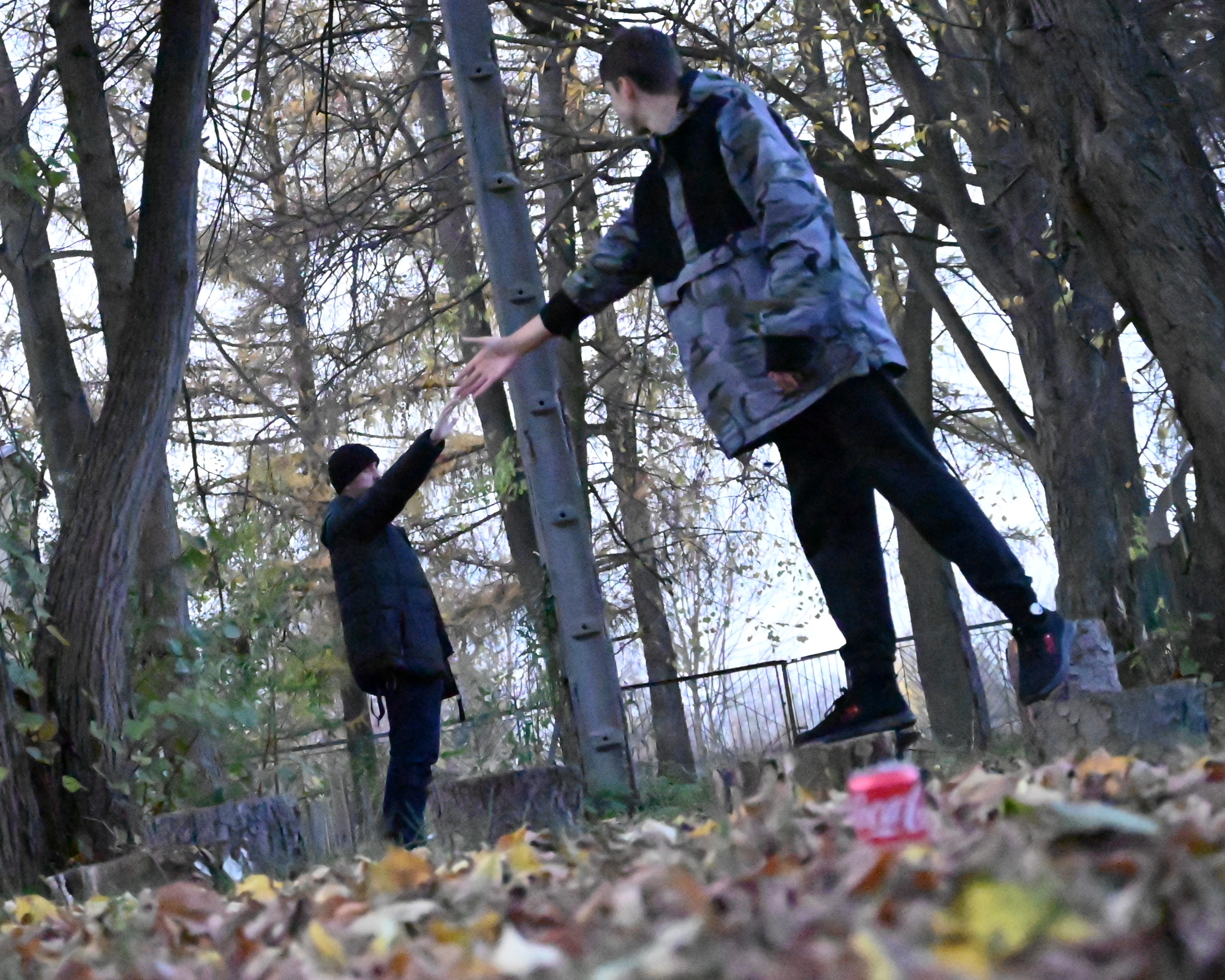 Cykl zajęć z programu „Fajna ferajna”  | Zdjęcie z użyciem perspektywy - jeden chłopiec stoi bokiem i wydaje się być bardzo duży, drugi, też bokiem - bardzo mały. Chłopcy wyciągają do siebie ręce. W tle pnie dużych drzew.JPG