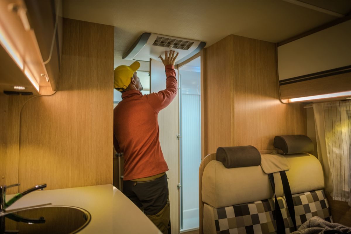 A man checking a vent in his RV as preventive maintenance, one of the best ways to save on RV travel