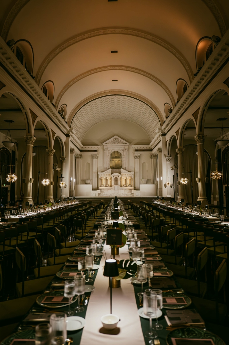 the Vibiana Main Hall in Downtown Los Angeles, lined with long rectangular tables with green table settings and square wine glasses