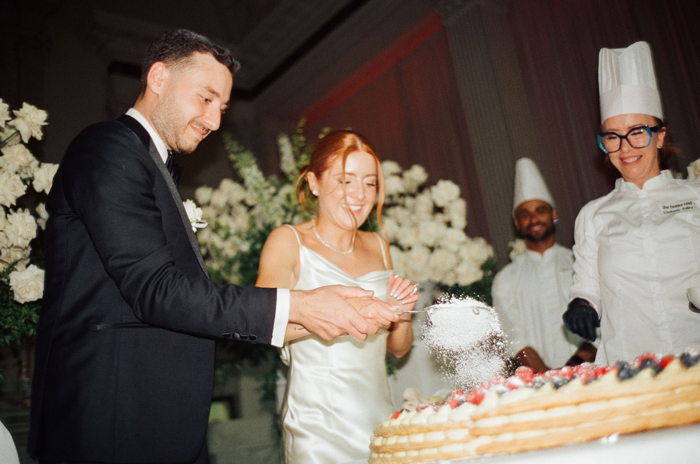 a bride and groom sift baking powder over their wedding cake