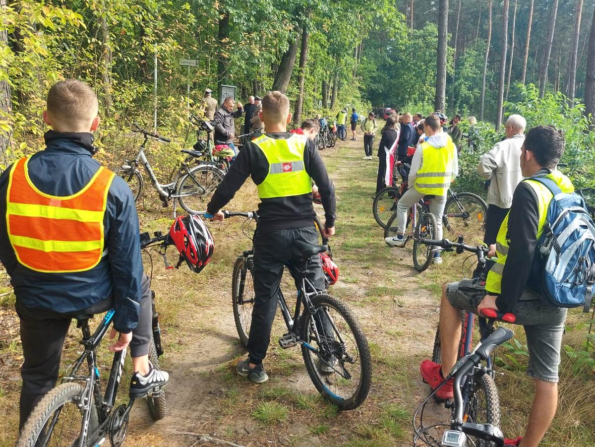 Rajd rowerowy | Wychowankowie MOW oraz inni uczestnicy rajdu widziani od tyłu ze swoimi rowerami na leśnej drodze..jpg