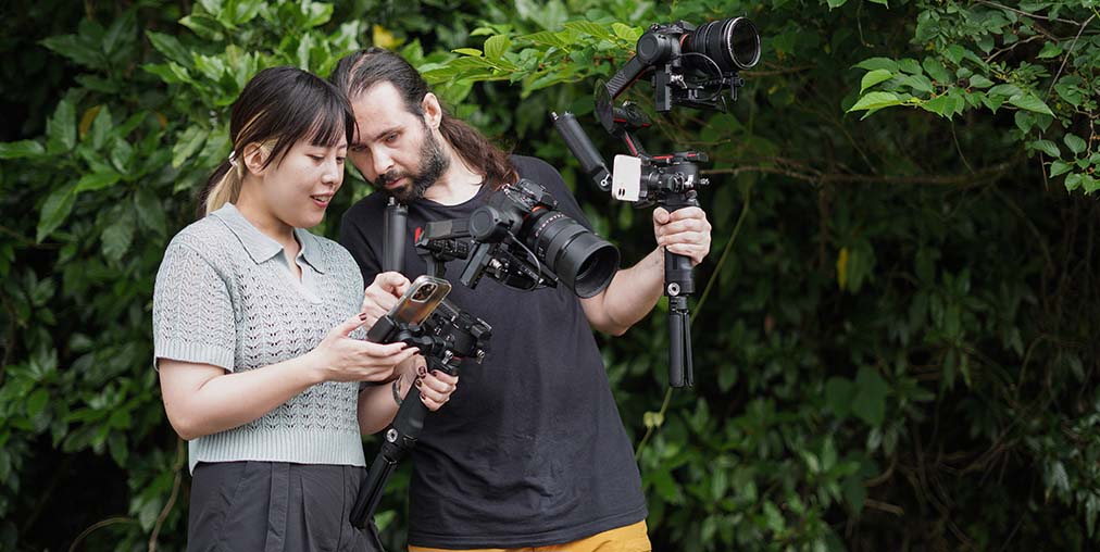 Man and woman filming outdoors with phone and professional camera