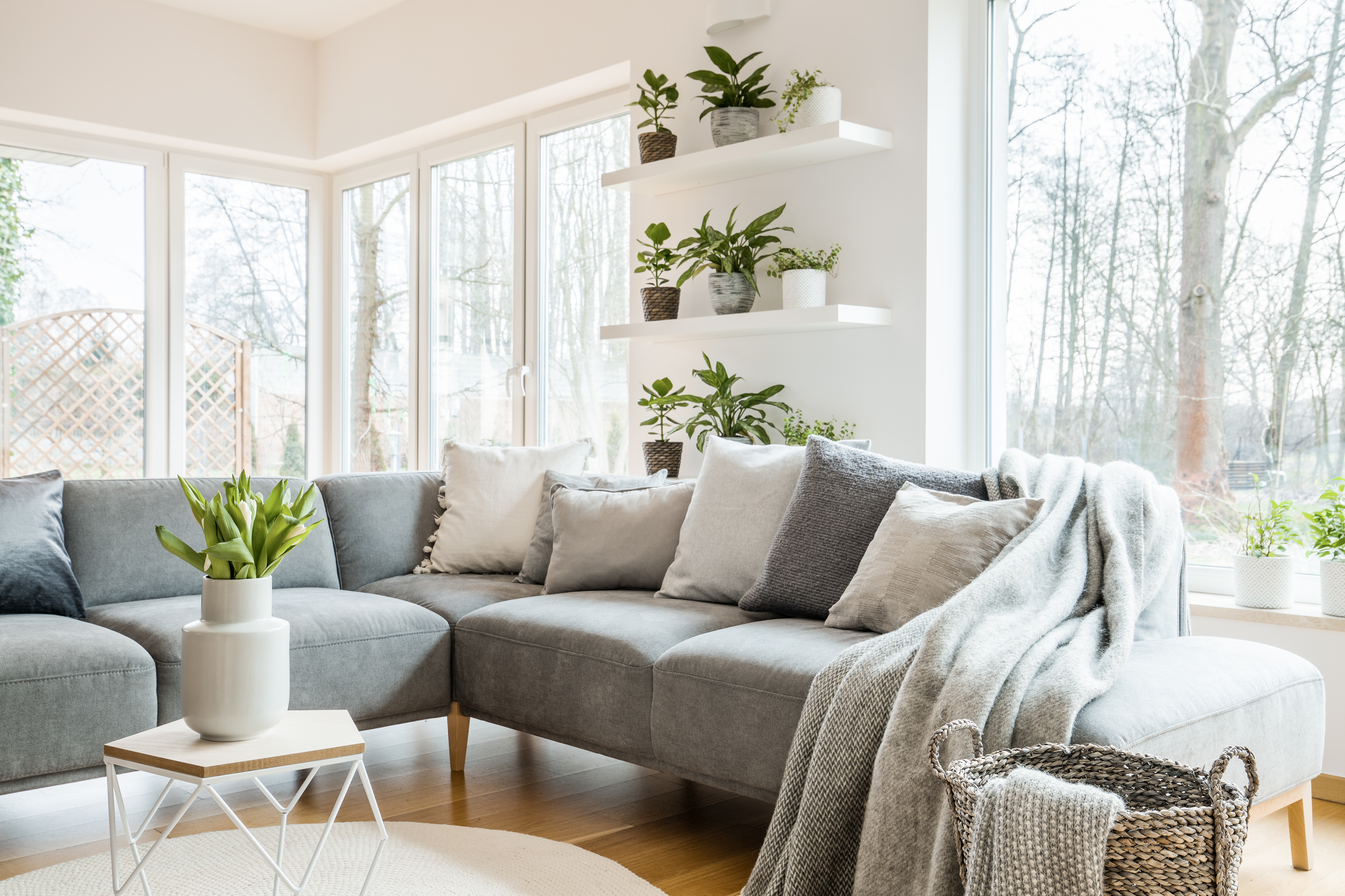 Grey corner couch with pillows and blankets in white living room interior