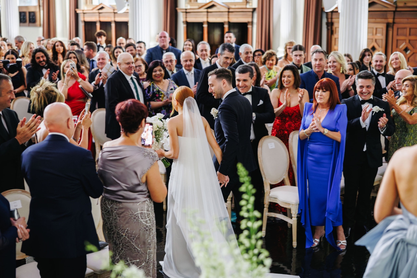 a newly married husband and wife walk down the aisle through the applause of their guests