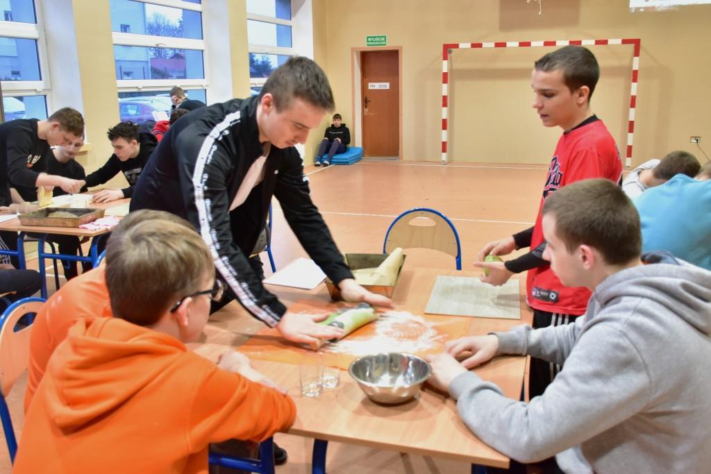 Dzień Św. Patryka  | Przy stole kilku chłoców robi ciasteczka, jeden wałkuje ciasto, inny wycina kółka. Na blacie miska, stolnica, podkładka.JPG