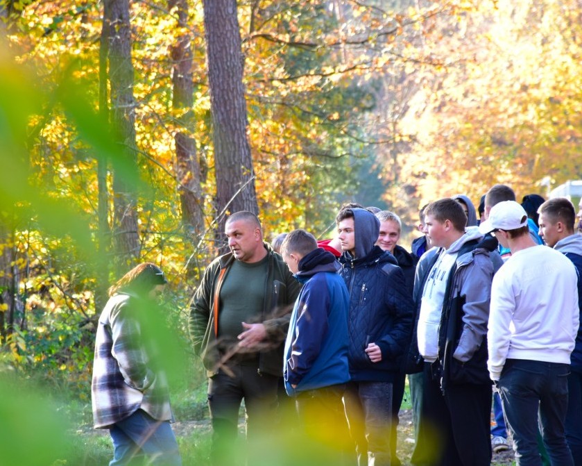 Zajęcia w szkółce leśnej | Grupa wychowankó MOW stoi między drzewami jesiennego lasu, przed nimi stoi leśniczy i jedna z wychowawczyń..JPG