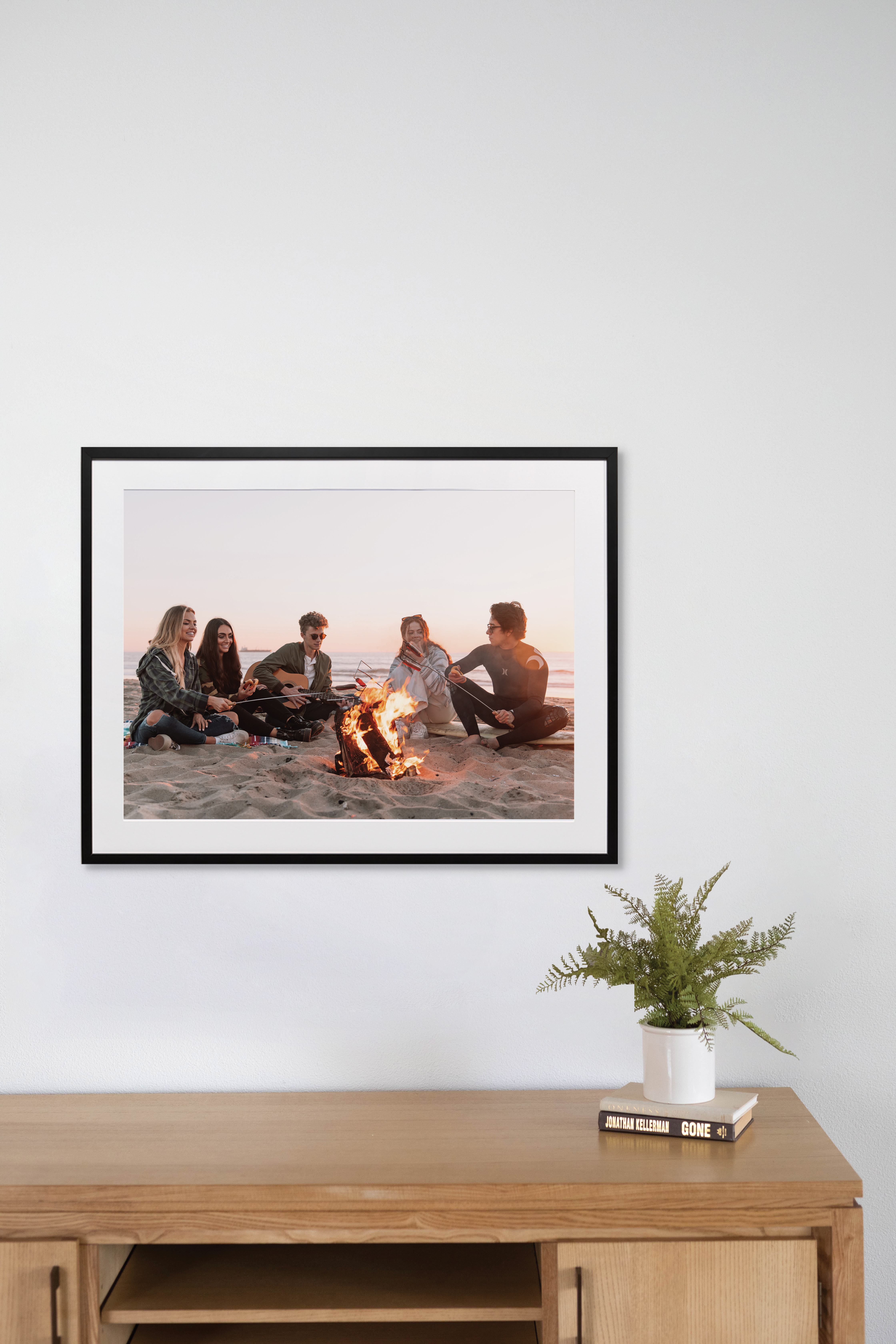 Framed print above desk of friends on the beach by the fire