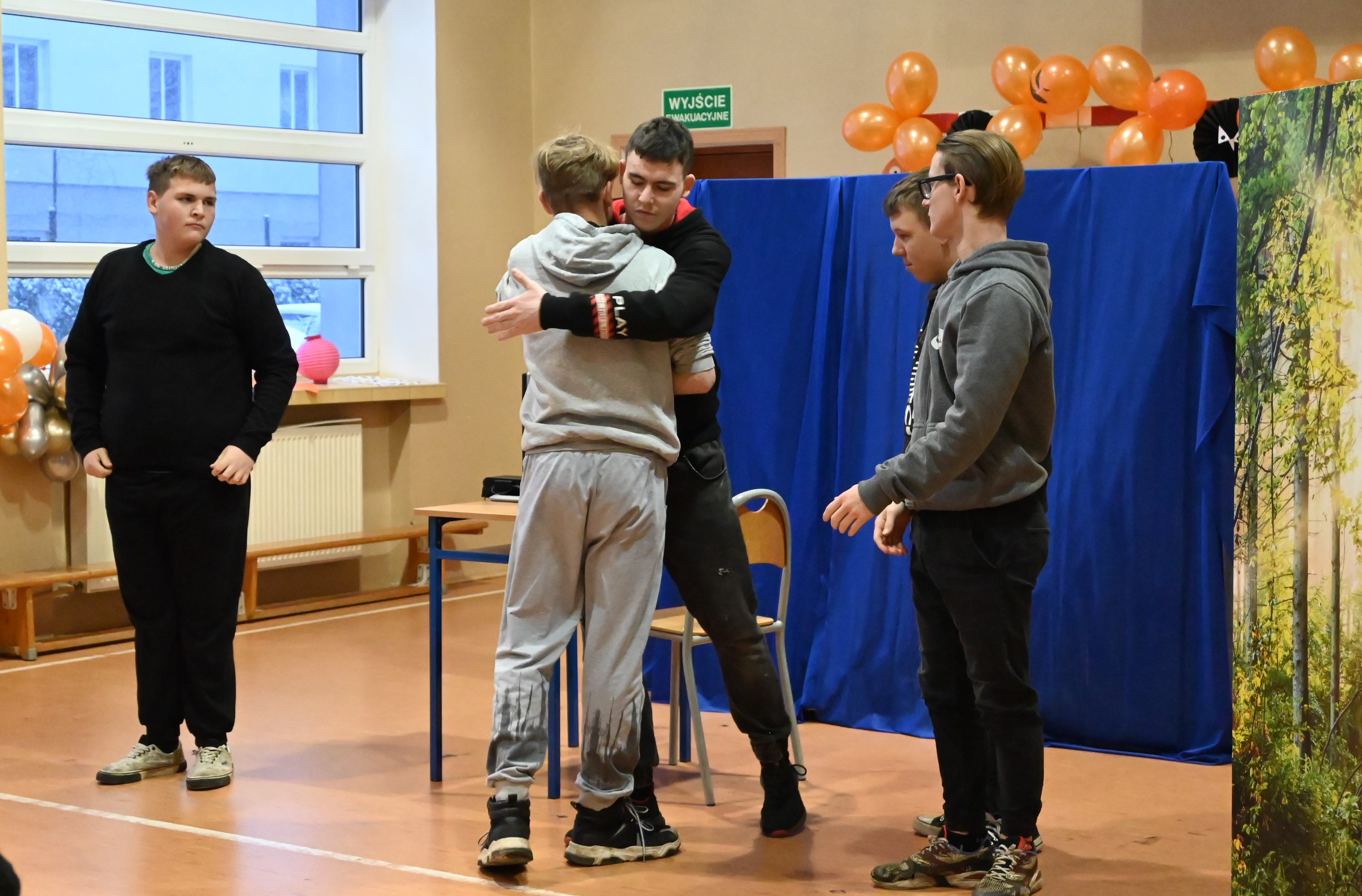 O uzależnieniach językiem teatru | Kadr z przedstawienia - dwóch chłopców przytula się, obok stoją inni dwaj chłopcy, z drugiej strony chłopiec ubrany na czarno patrzy w ich stron.JPG