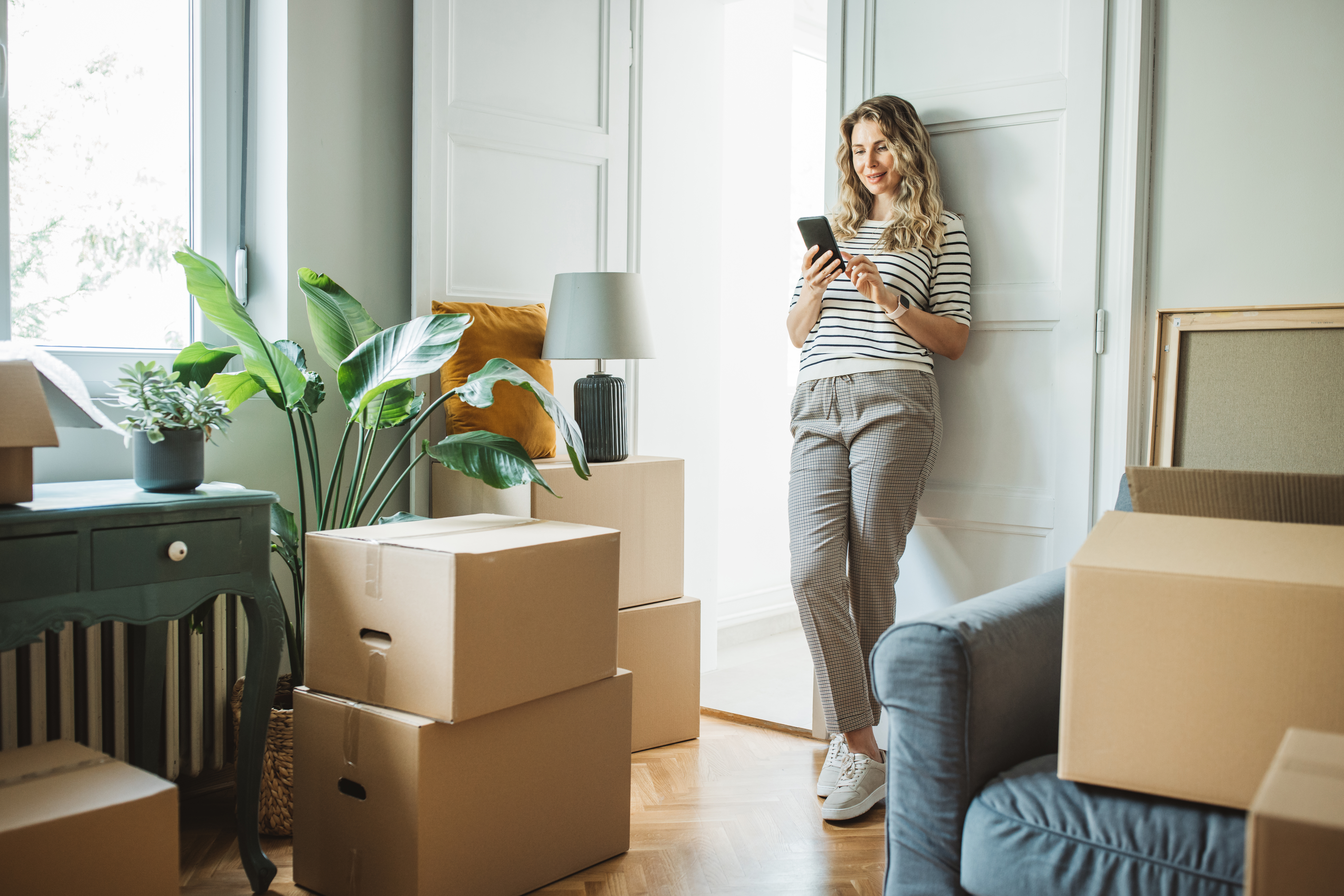 Woman scrolling through phone and unpacking boxes