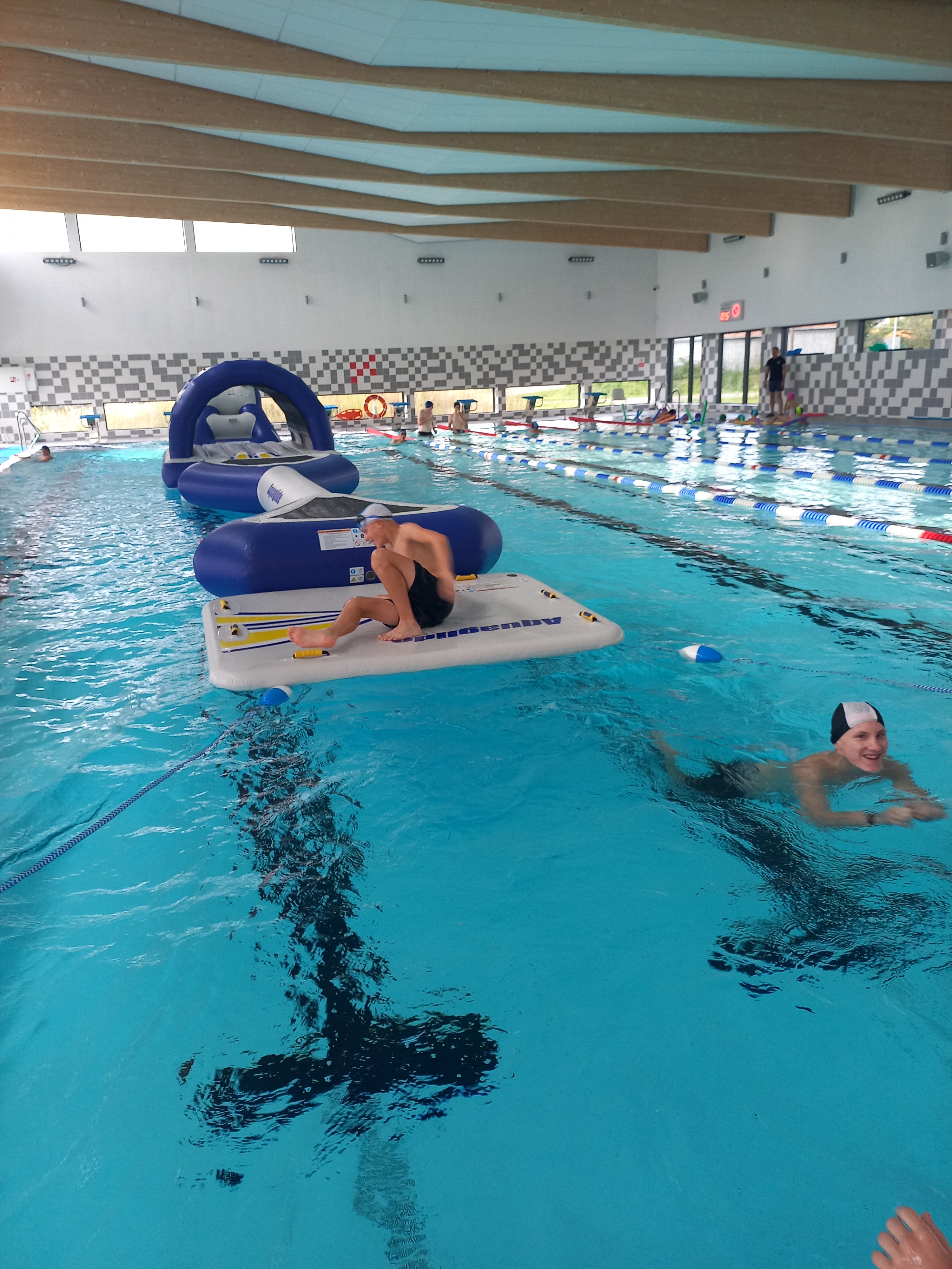 Zajęcia na basenie | Wychowanek MOW przygotowuje się do przejścia nadmuchiwanego toru przeszkód siedząc na platformie startowej, obok pływa inny wychowanek..jpg