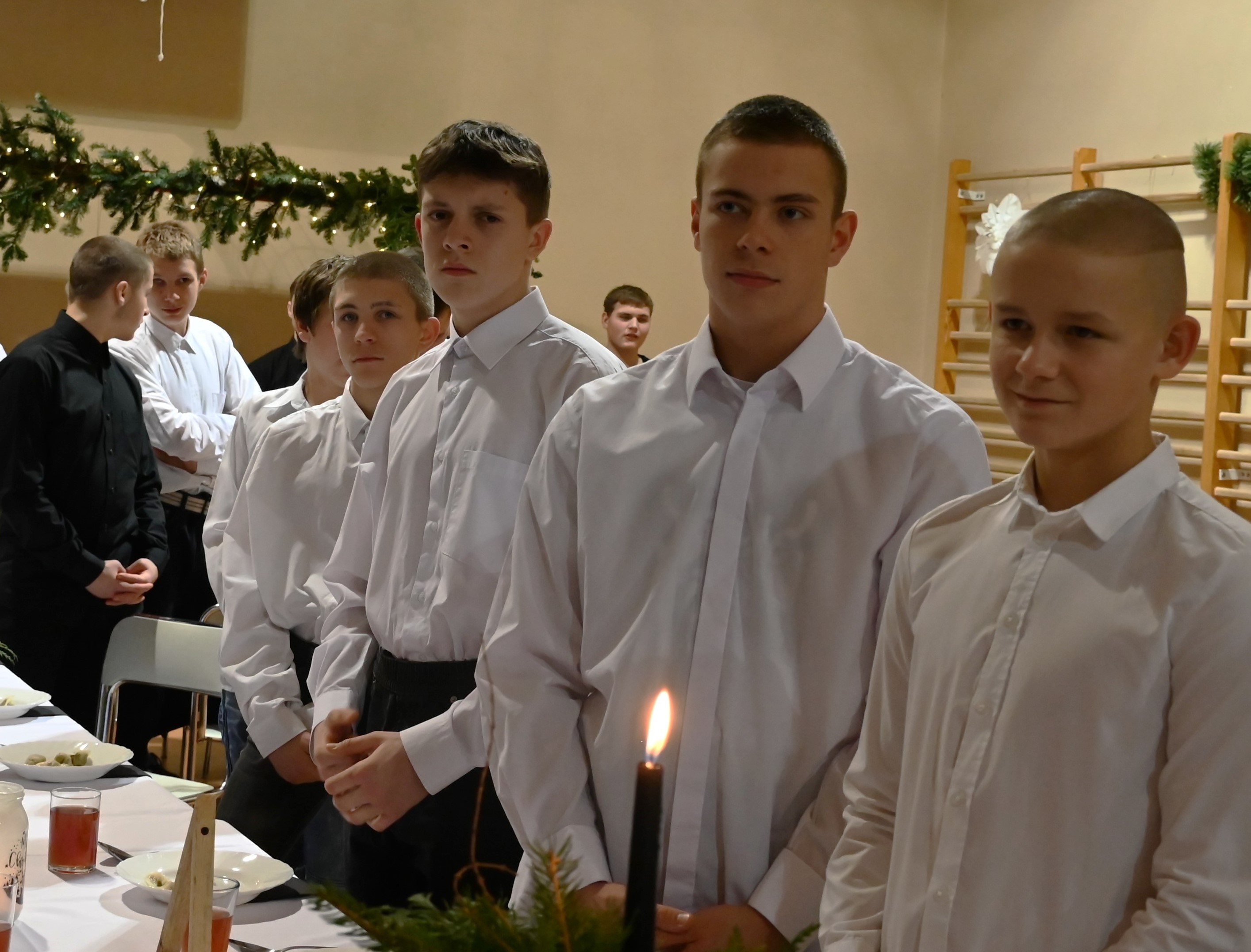 Wigilia w Ośrodku | Kilku chłopców w białych koszulach stoją rzędem za nakrytym do kolacji wigilijnej stołem.JPG