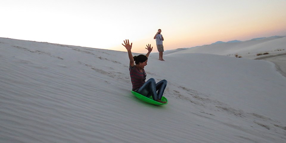 Woman riding a round sled down a sand dune at White Sands National Park in New Mexico
