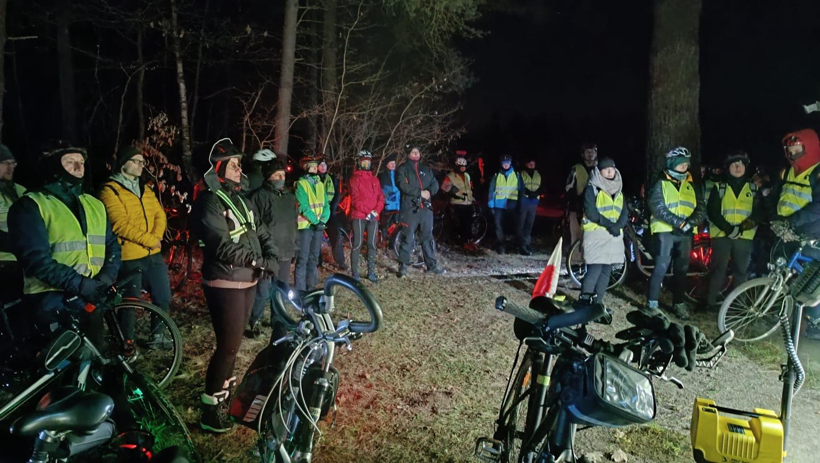 Rowerowa Droga Krzyżowa | Grupa kolarzy stoi w półkolu, modli się. Z przodu zaparkowane rowery, w tle las. Zdjęcie nocne.jpg