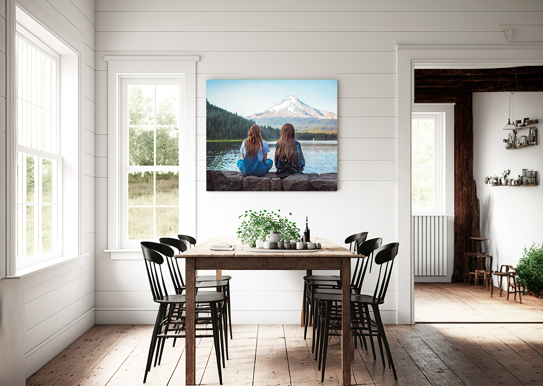 Large metal print in the dining room of two girls sitting by the water and mountains