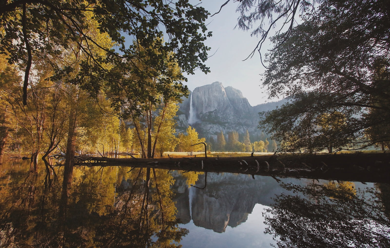 Autumn scene of pond with colorful trees and mountains in the background.