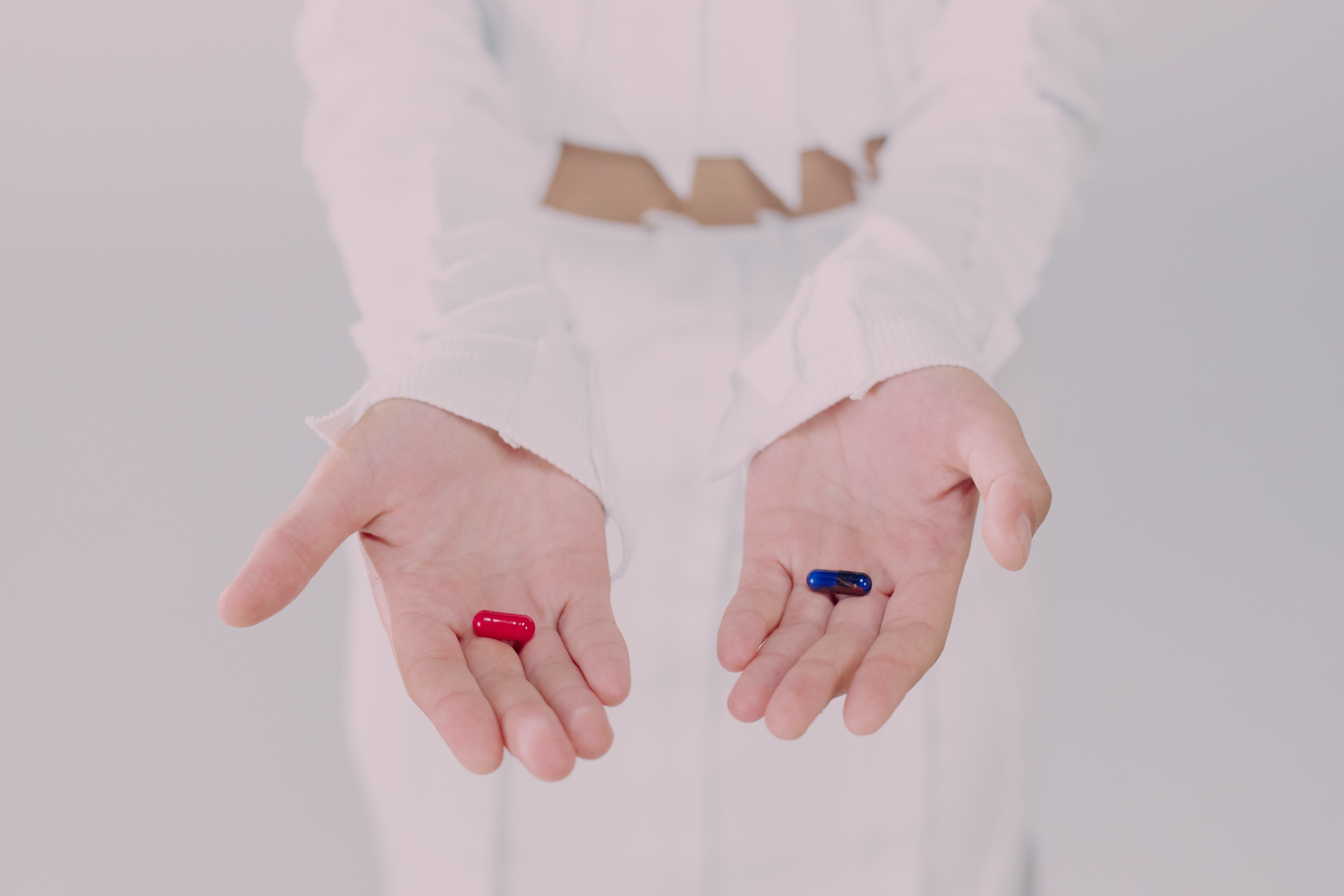 Tabletki w kolorze czerwonym i niebieskim podane na dłoniach
