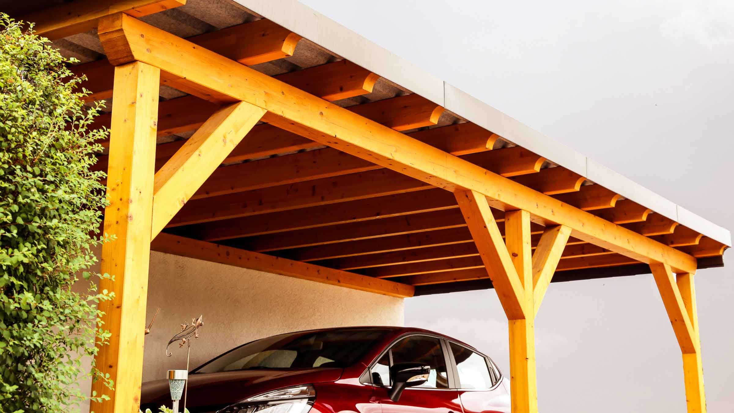Sturdy wooden framed carport with corrugated rooftop and a red car parked beneath it.