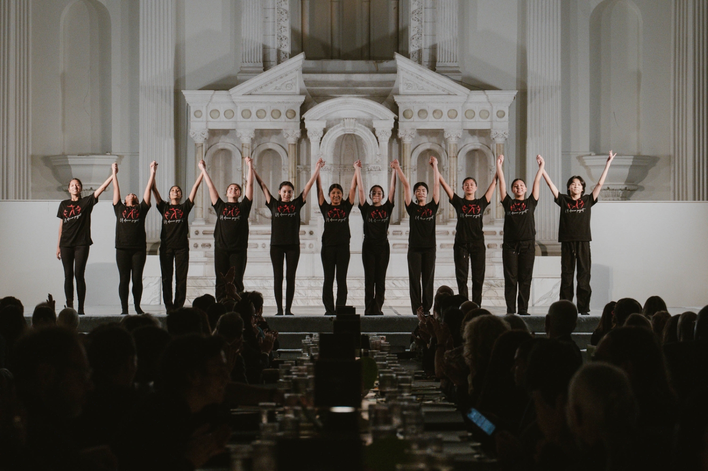 a group of young dancers hold hands and hold up their arms as they bow towards the audience at a performance gala in downtown Los Angeles