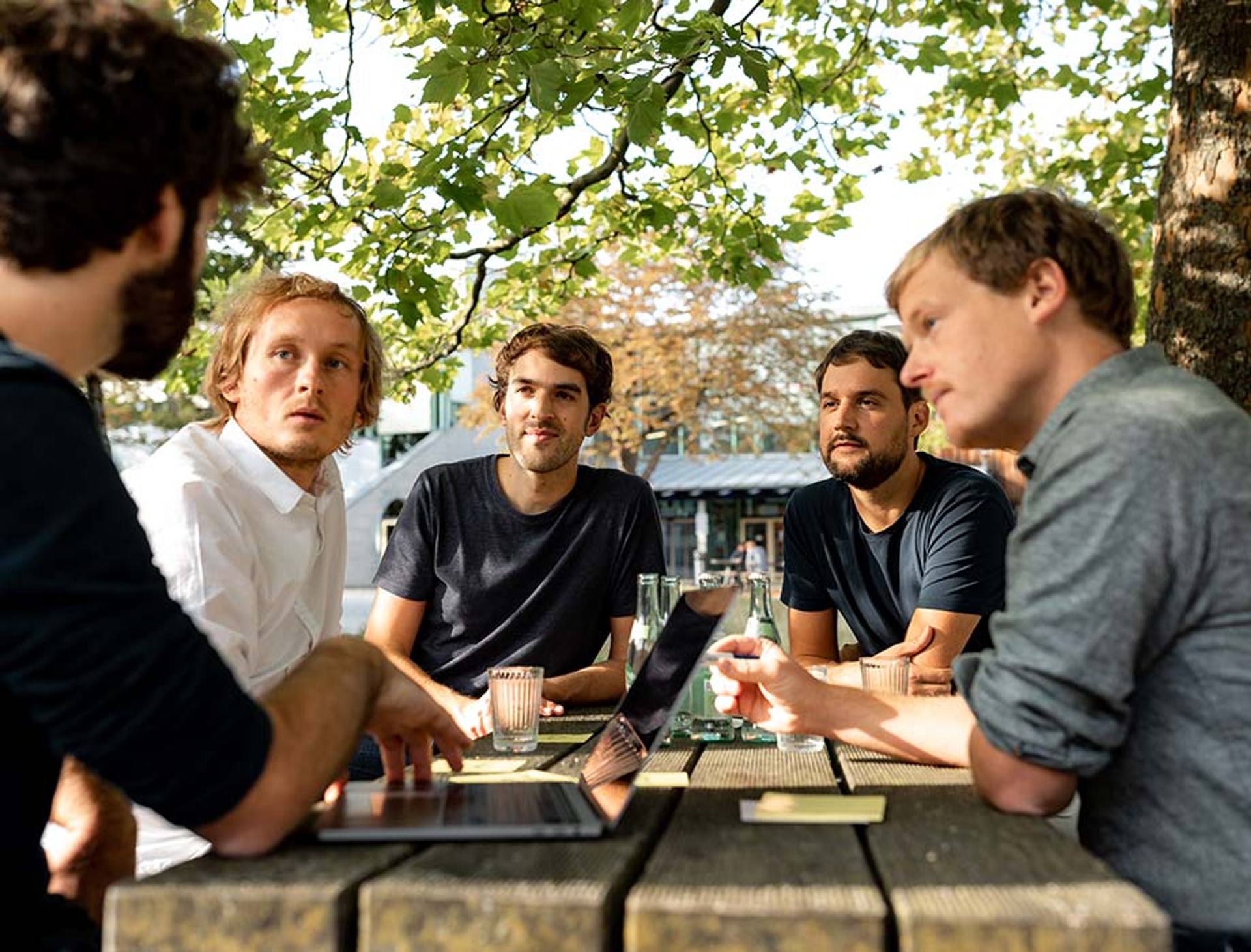 The founders of the Peerigon software company at a table under a tree