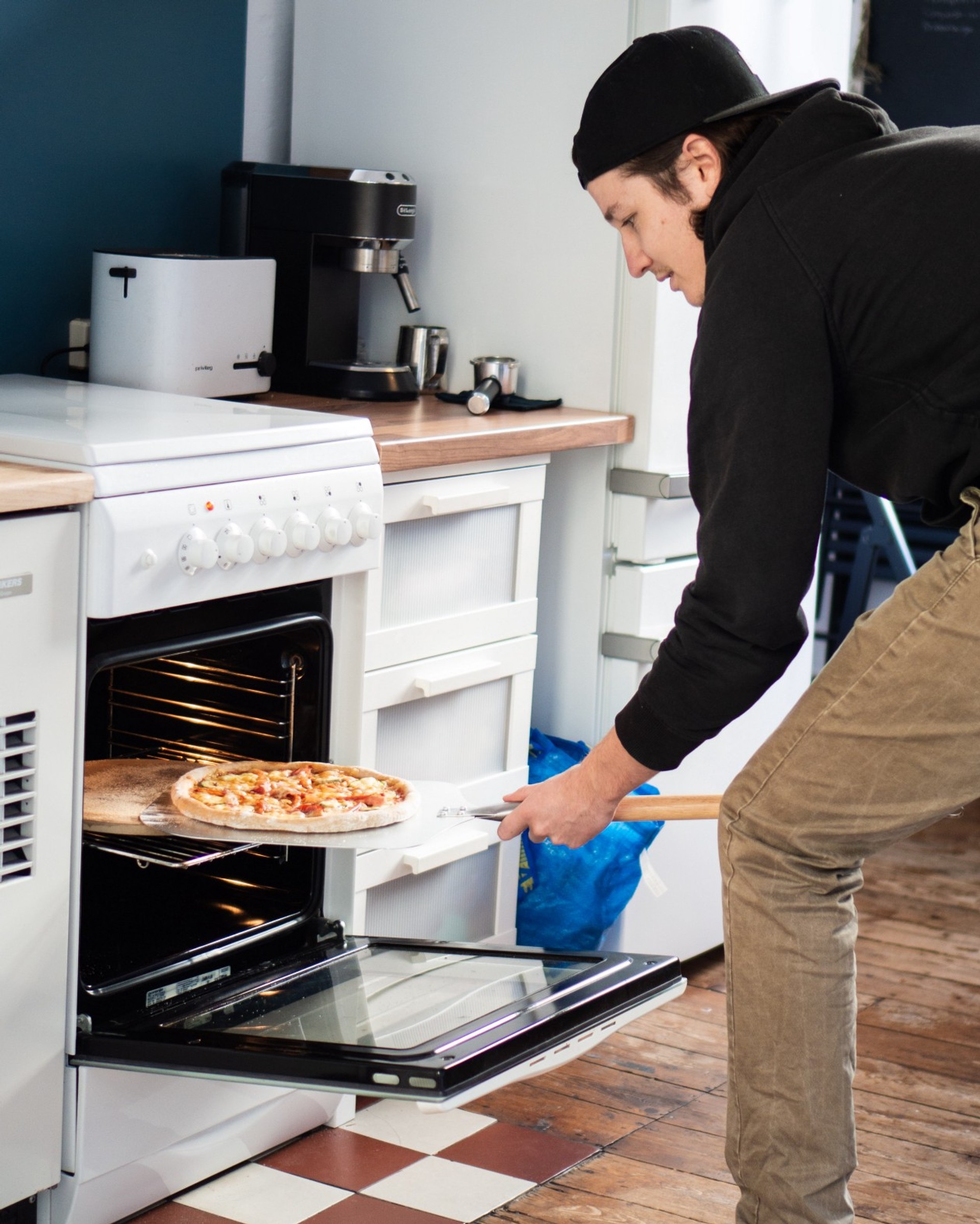 a young man in a kitchen getting a pizza out of the oven