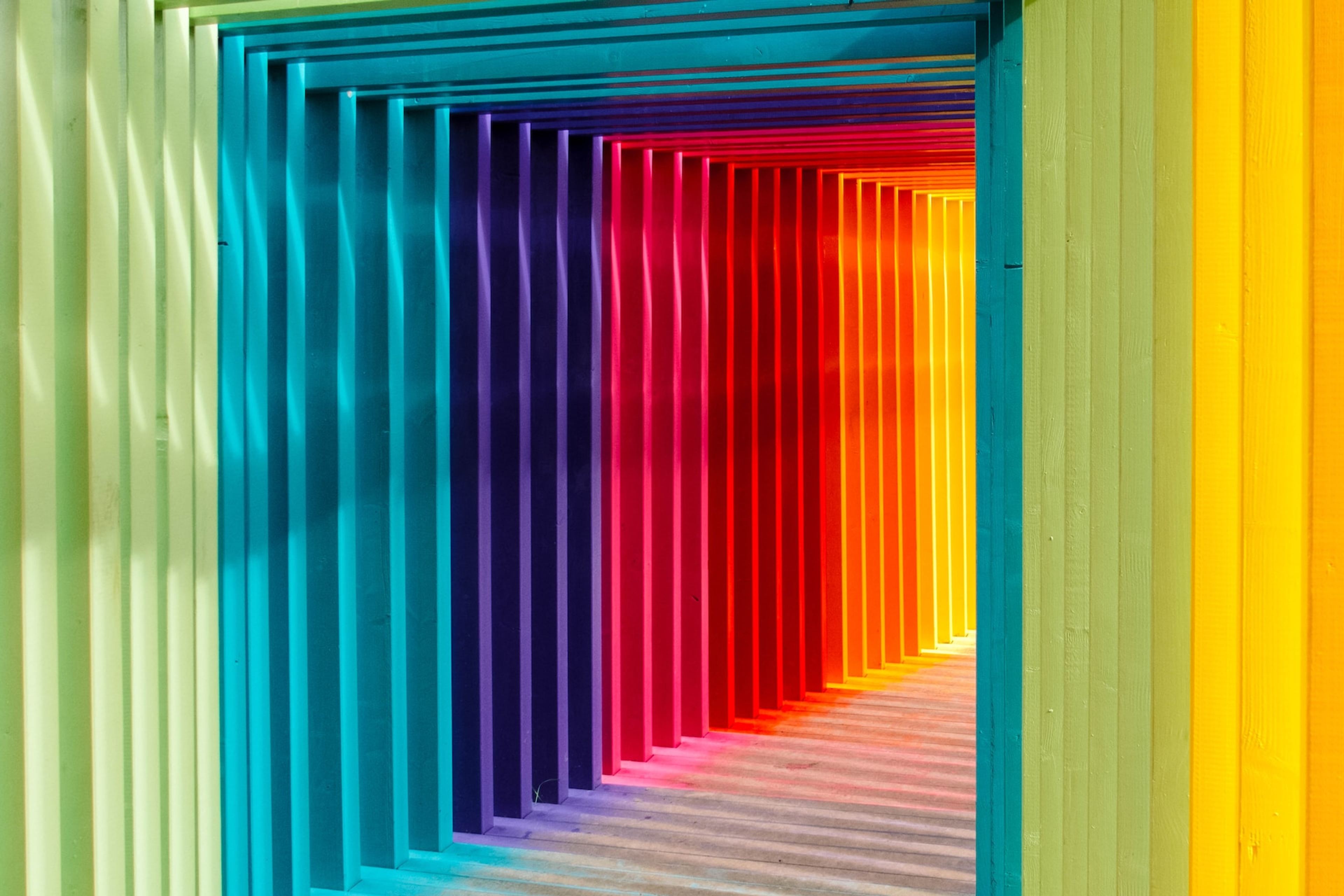 hallway of wood in rainbow colors with sunlight shining in between the planks