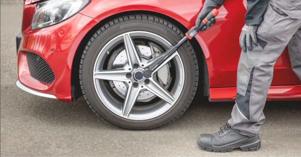 Man (right) uses new WÜRTH Premium torque wrench on the front wheel of a red car.