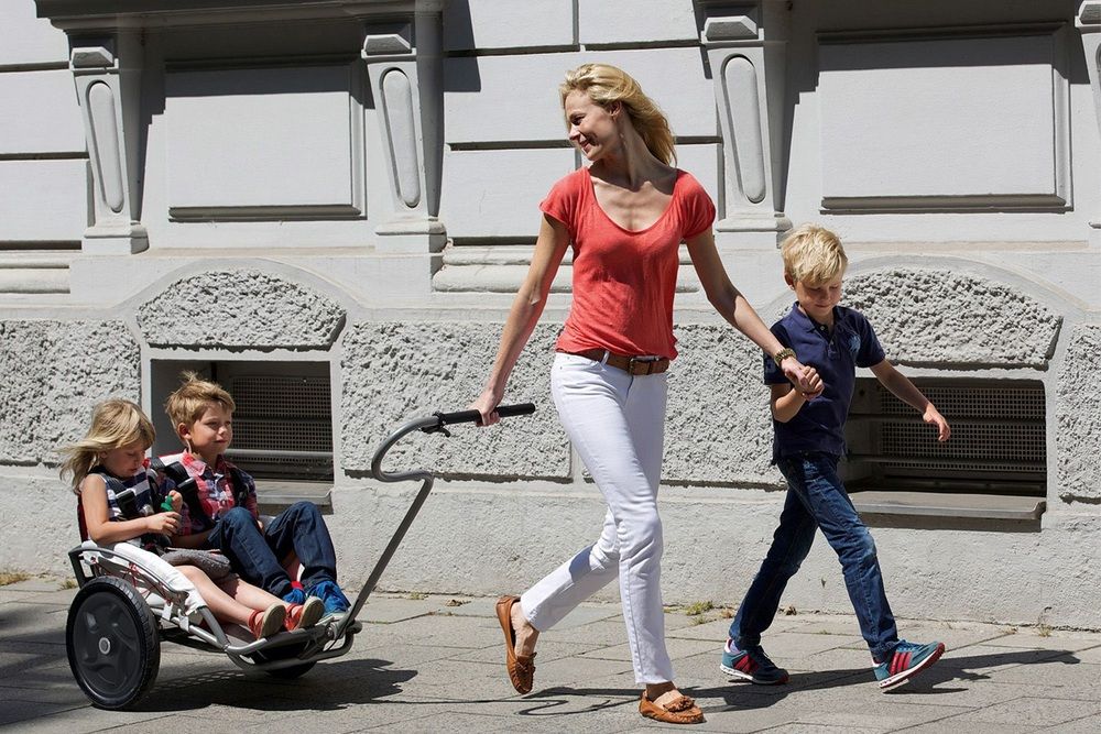 Mother pulling stroller with two children in it through the city