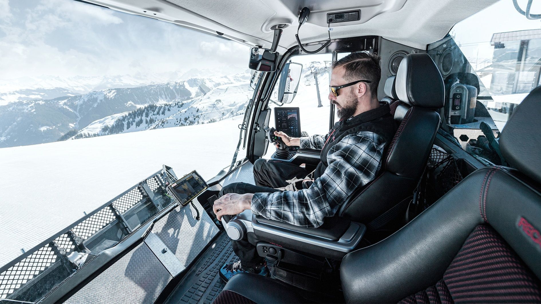 Man drives snow groomer in snow-covered mountains