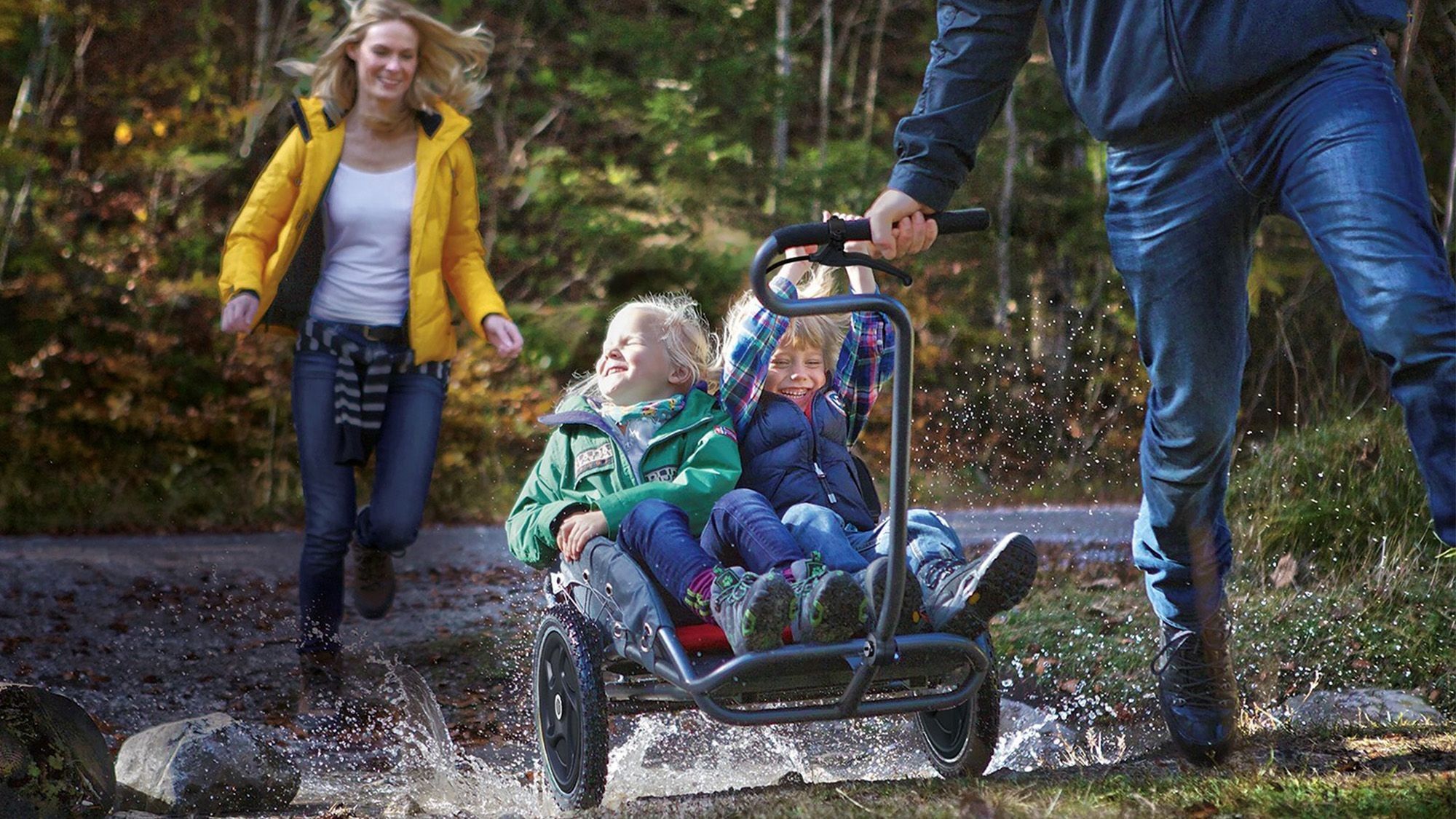 Two children sitting in a baby carriage being pulled through the forest
