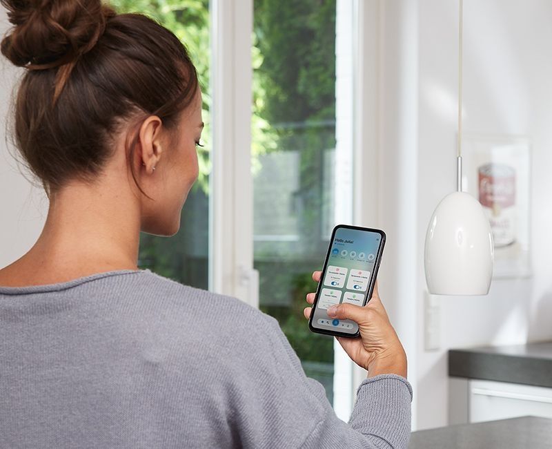 Woman holding a smartphone with the SIEGENIA HomeConnect app open in her right hand.