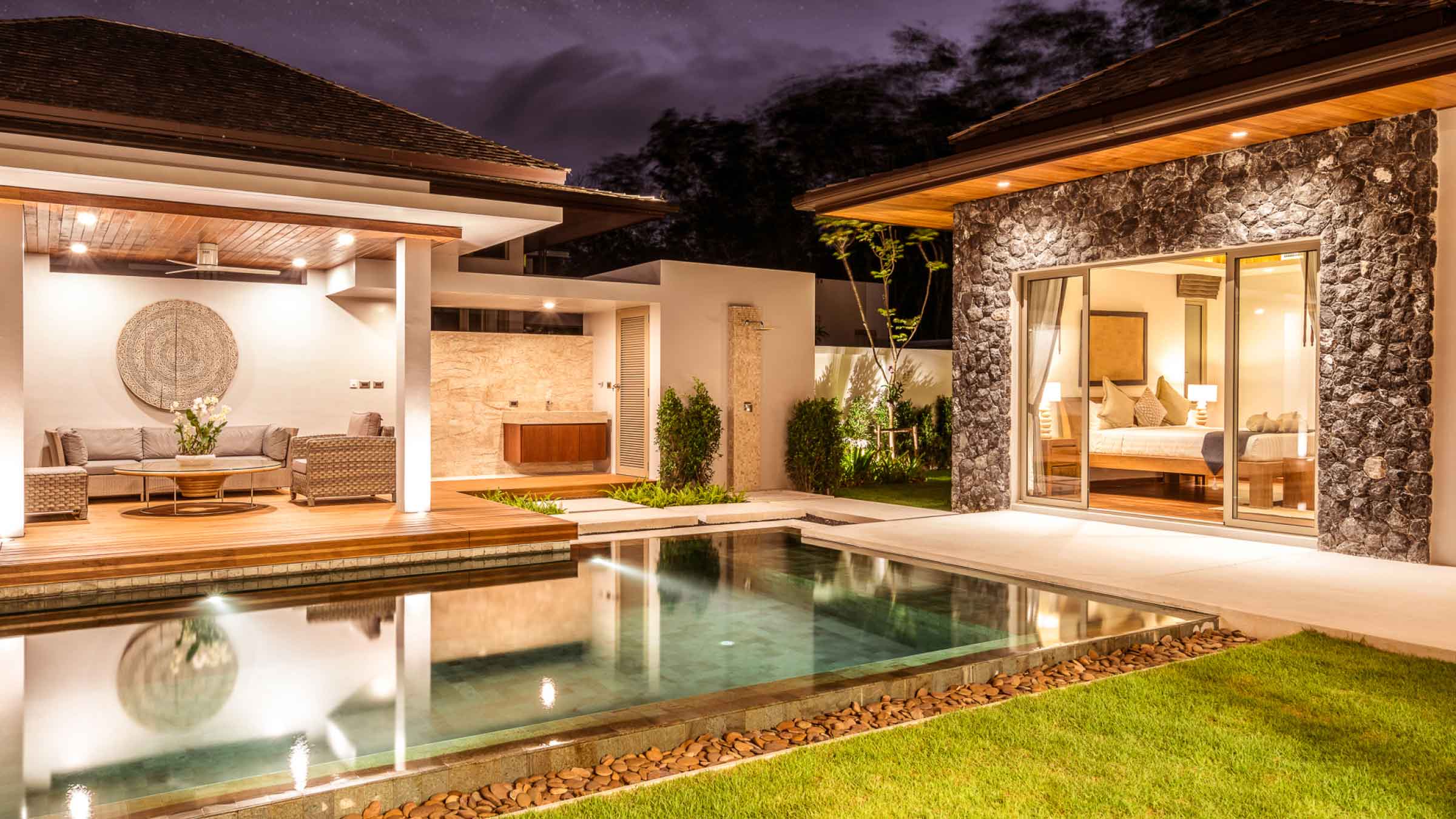 Modern luxury backyard, with a pool and entertainment area. Lit up at night with warm soft lighting.